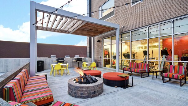 An outdoor patio with a fire pit, colorful striped seating, and a covered area with string lights. - Home2 Suites by Hilton Columbus Downtown (Columbus)
