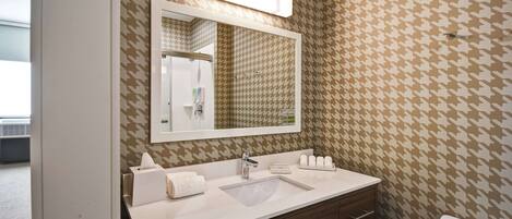 A bathroom with a houndstooth patterned wall, a large mirror, a white sink, a vanity with a mirror, and a toilet.