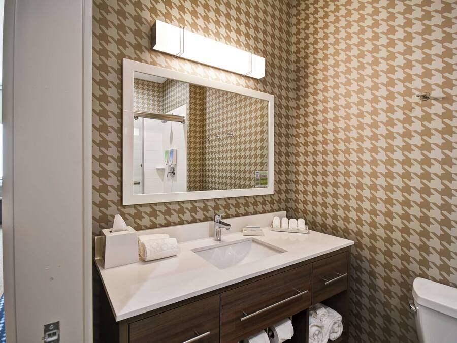 Un baño con pared de estampado pata de gallo, un espejo grande, un lavamanos blanco, un tocador con espejo y un inodoro.