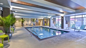 Una piscina cubierta con vistas claras al área de la piscina, un espacio de descanso con sillas y vistas al exterior a través de grandes ventanales.
