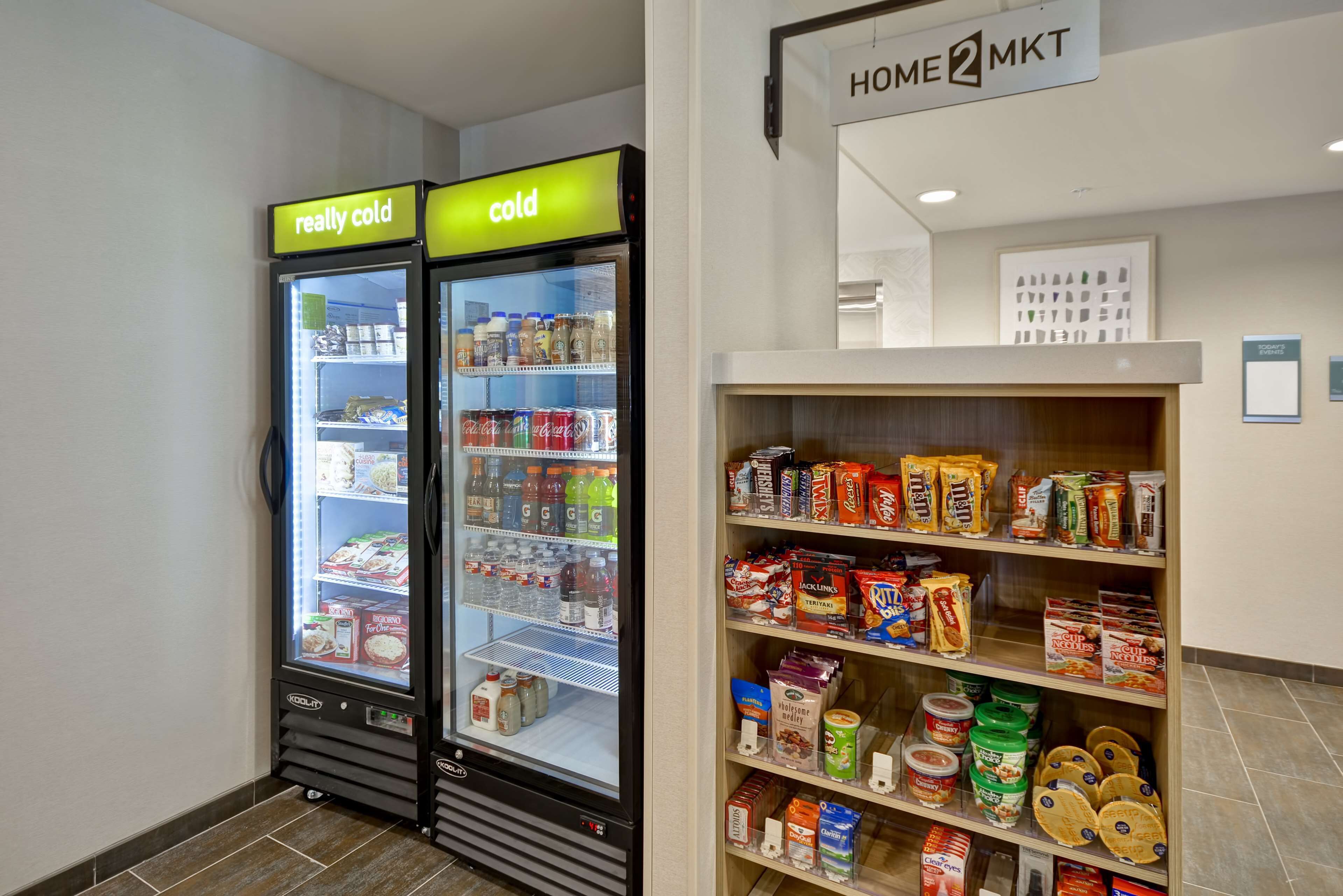 A vending machine area with two refrigerated units labeled "really cold" and "cold," and a shelf stocked with various food items and beverages.
