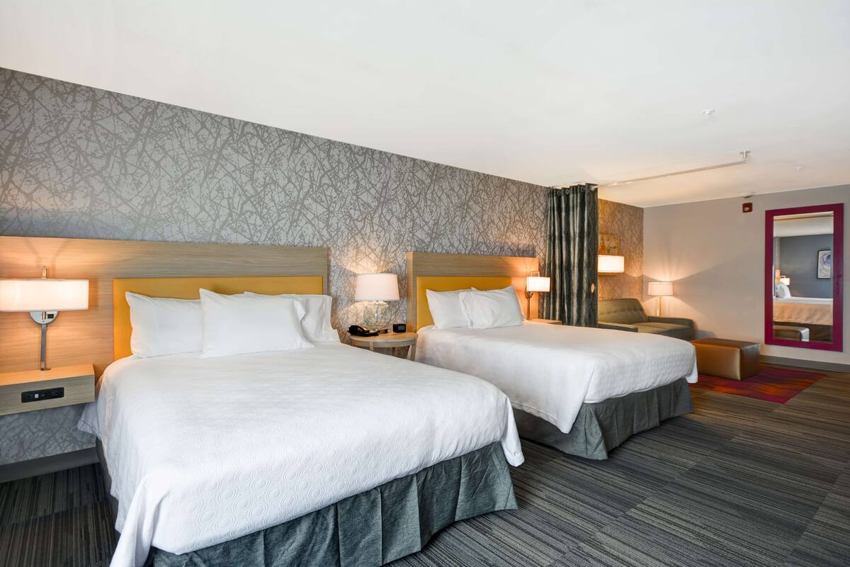 A hotel room with two beds, nightstands with lamps, a mirror, and a patterned wall.