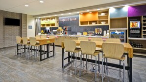 Un restaurante moderno con varias mesas y sillas, una barra con menú y una pantalla de televisión.