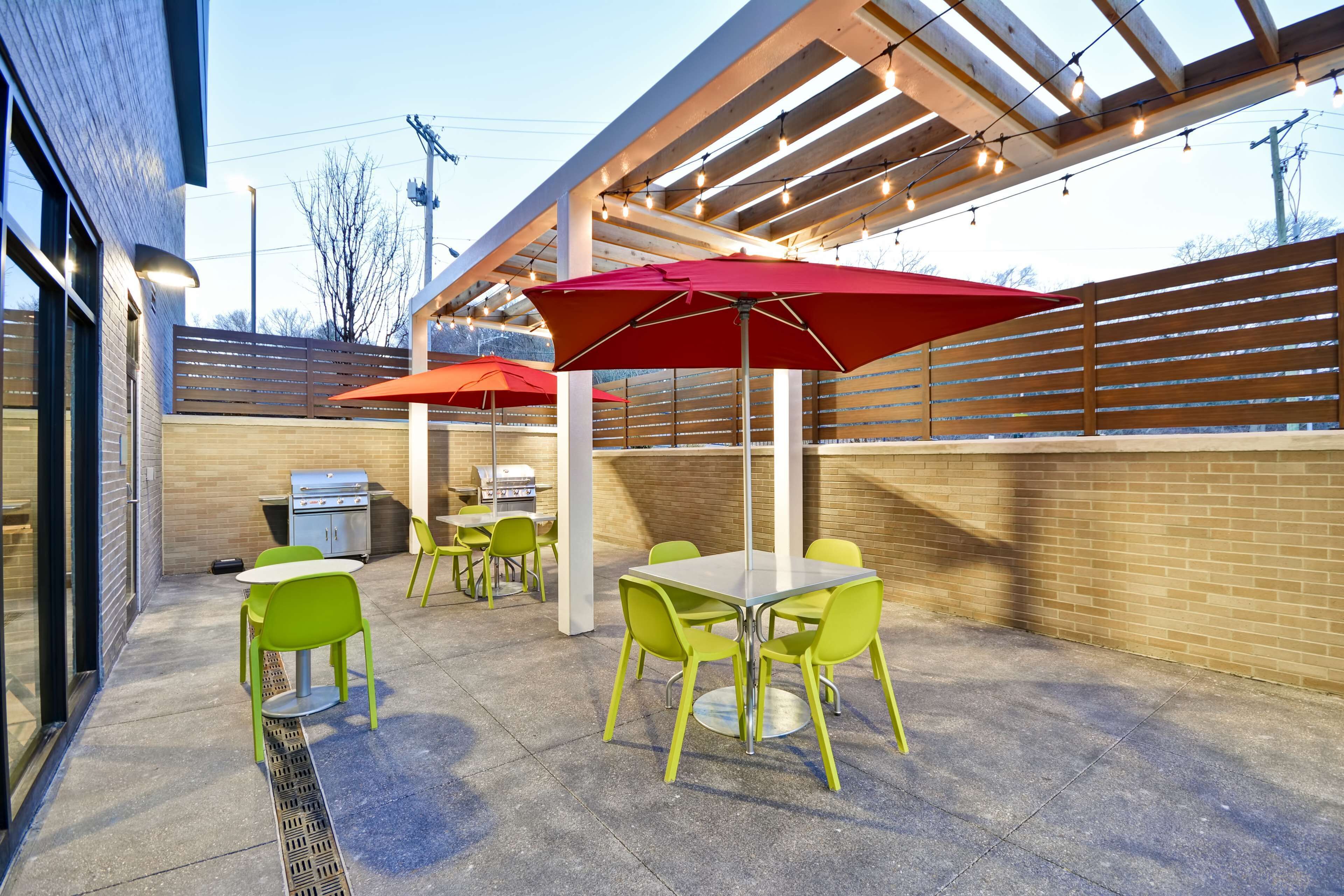 An outdoor patio area with tables and chairs, a barbecue grill, and string lights.
