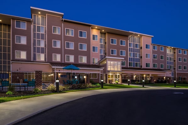 A multi-story hotel with a modern design, featuring a covered outdoor seating area and a well-lit entrance.