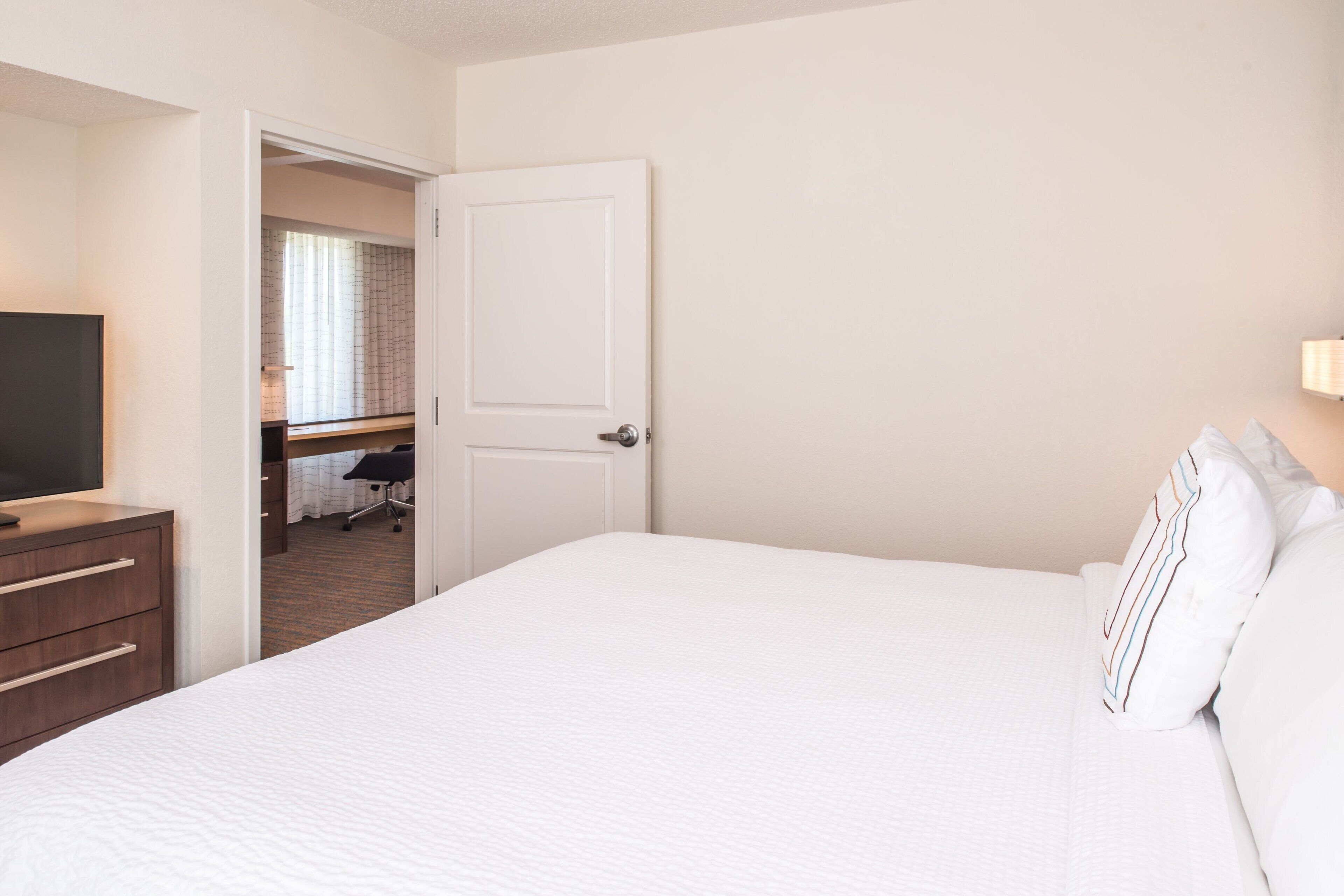 A hotel room with a large bed, a TV on a wooden dresser, and a door leading to a bathroom.