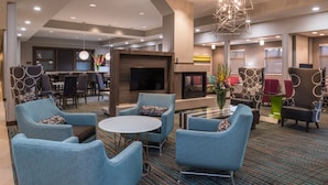 A modern hotel lobby with blue armchairs, a round table, a fireplace, and a television. - Residence Inn by Marriott Decatur (Decatur)