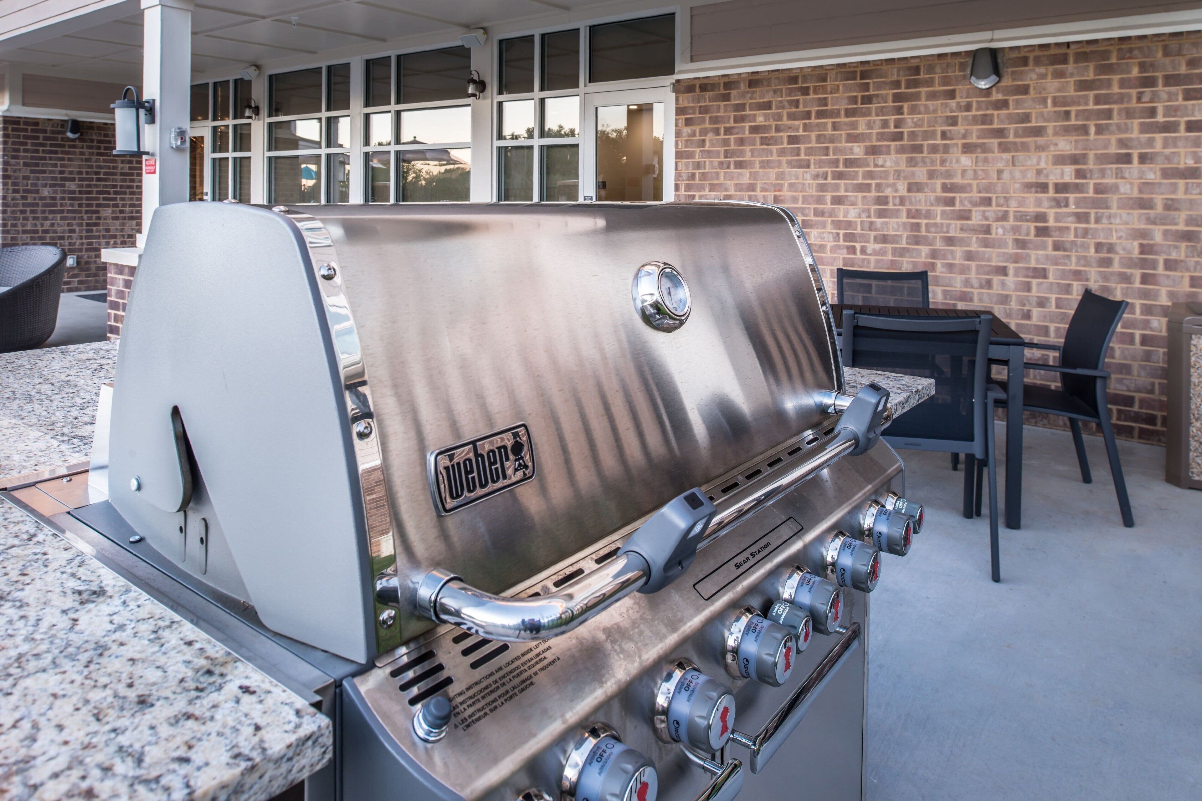 Ein Weber-Grill mit mehreren Bedienelementen, eine Ziegelwand und Sitzgelegenheiten im Freien.