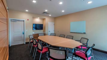Un salón de conferencias con una gran mesa, sillas, una pizarra y una televisión.