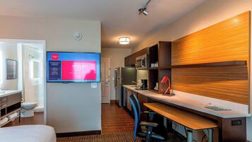 A hotel room with a bed, a desk with a computer, a TV, a microwave, and a refrigerator.
