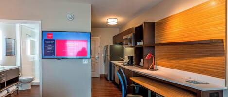 Habitación de hotel con cama, escritorio con computadora, televisor, microondas y refrigerador.