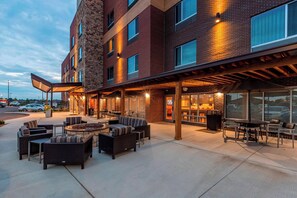 An outdoor seating area with wicker furniture and a fire pit, adjacent to a building with large windows and a brick facade. - TownePlace Suites by Marriott Lexington Keeneland/Airport (Lexington)
