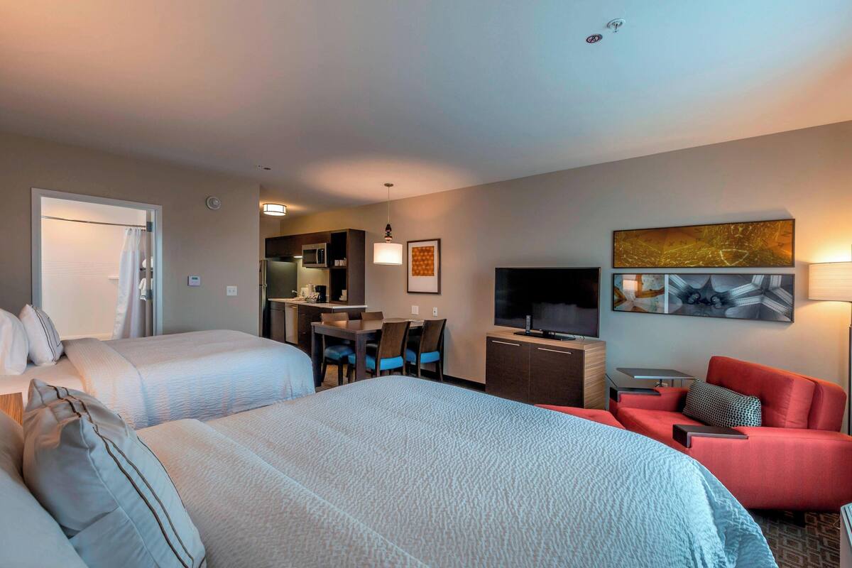 Ein Hotelzimmer mit zwei Betten, einem Schreibtisch mit Stuhl, einem Fernseher und einem roten Sofa.