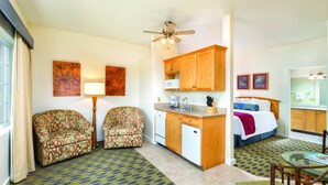 A compact hotel room with a kitchenette, two patterned armchairs, a bed with a colorful blanket, and artwork on the walls. - Worldmark Cathedral City (Cathedral City)