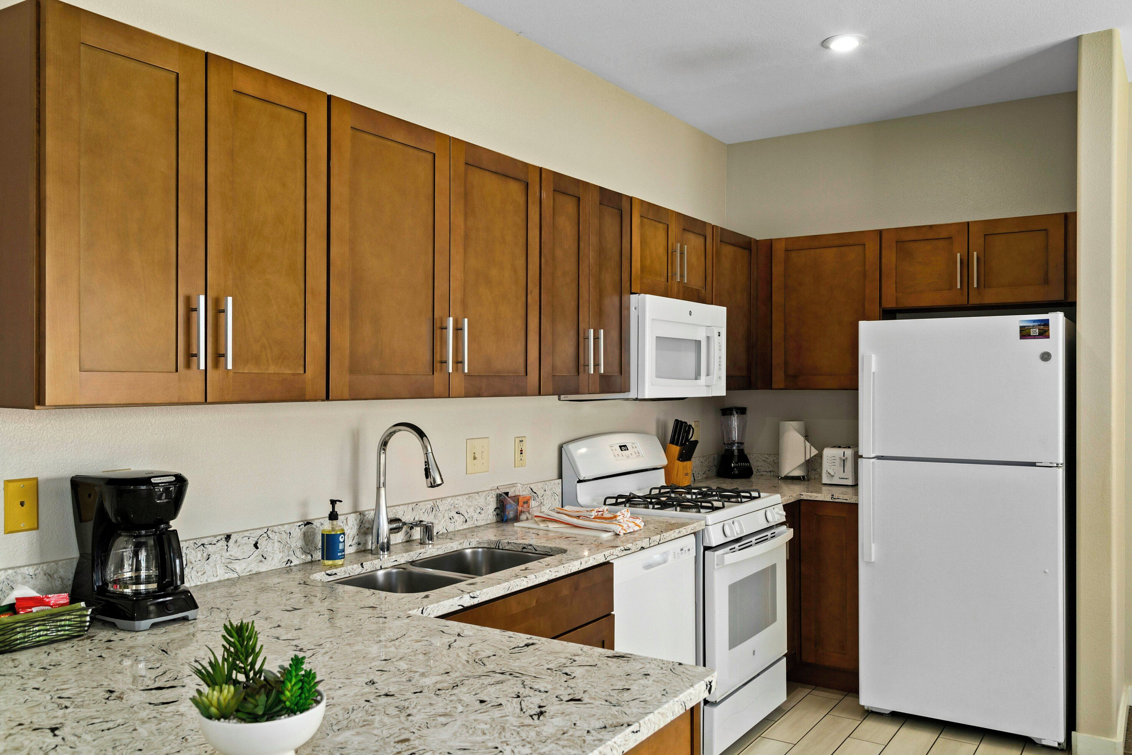 A kitchen with wooden cabinets, a stainless steel sink, a built-in microwave, a gas stove, and a white refrigerator.