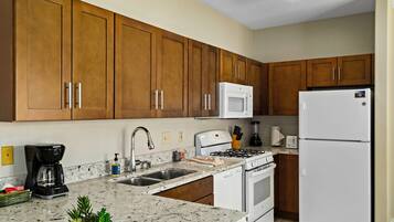 A kitchen with wooden cabinets, a stainless steel sink, a built-in microwave, a gas stove, and a white refrigerator.