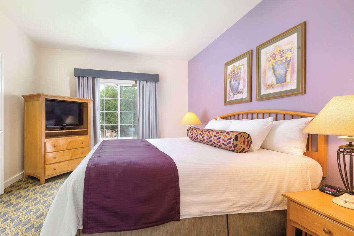 A hotel room with a bed, a TV, a lamp, and two paintings on the wall.