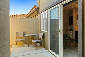 A small patio area with two wicker chairs and a round table, a sliding glass door leading to an interior space, and a tiled roof above. - Worldmark Cathedral City (Cathedral City)