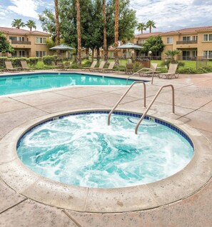 A hot tub surrounded by lounge chairs and a pool, with a building in the background. - Worldmark Cathedral City (Cathedral City)