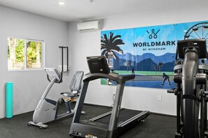 Une salle de sport équipée de matériel d’exercice, ornée d’une fresque murale et dotée d’une fenêtre donnant sur des arbres.