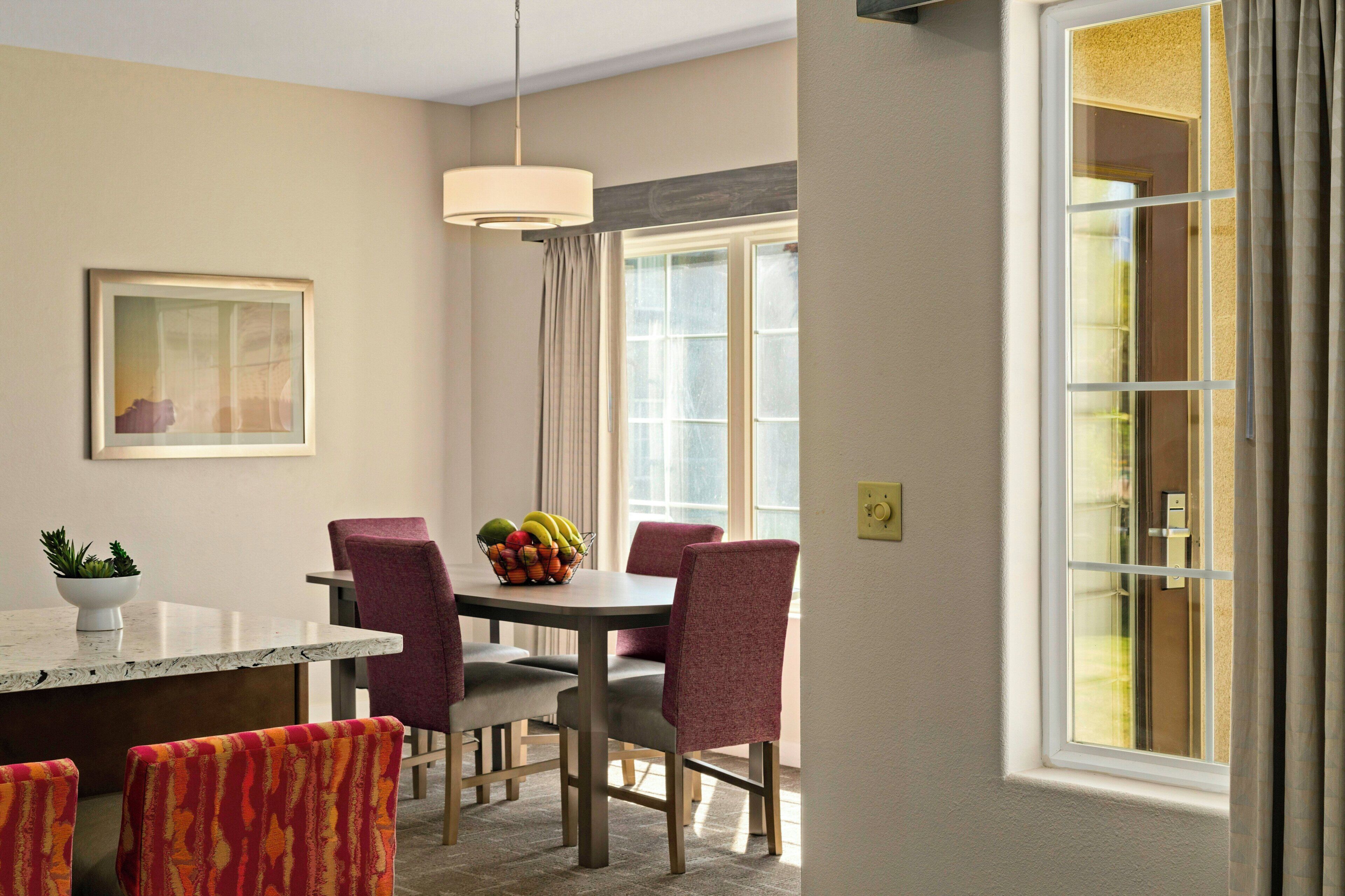 A dining area with a table, chairs, a fruit bowl, and a pendant light.
