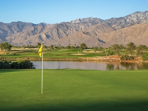 A golf course with a flag, water body, and mountains in the background. - Worldmark Cathedral City (Cathedral City)