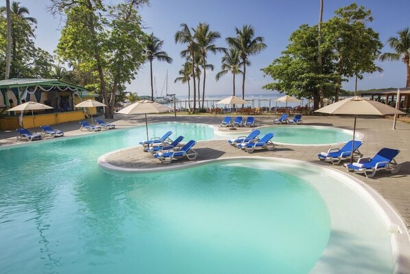 A pool area with blue lounge chairs and umbrellas, surrounded by palm trees and a clear sky. - whala boca chica (Boca Chica)