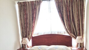 A bedroom with a bed, two nightstands, a window with curtains, and a view of the city. - Alto San Isidro (Santiago)