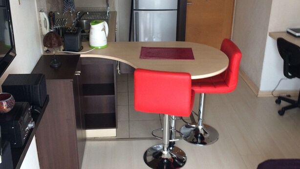 A compact kitchen with a microwave, refrigerator, and a sink. There is a small dining area with a red chair and a table. - Alto San Isidro (Santiago)
