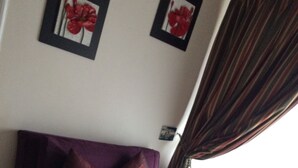 A purple sofa with two pillows, a small round table with a red object, and a window with curtains. - Alto San Isidro (Santiago)