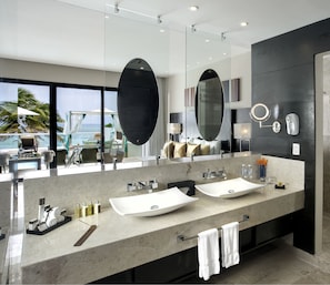 Un baño moderno con un espejo grande, dos lavamanos y vistas al océano.