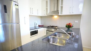 A modern kitchen with stainless steel appliances, a granite countertop, and white cabinetry. - Premiere Apartments (Nadi)