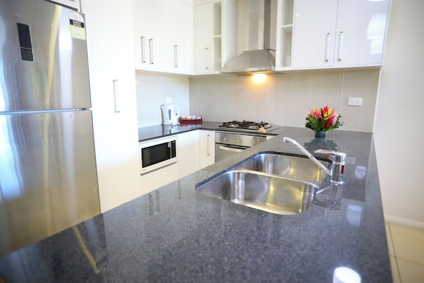 A modern kitchen with stainless steel appliances, a granite countertop, and white cabinetry. - Premiere Apartments (Nadi)
