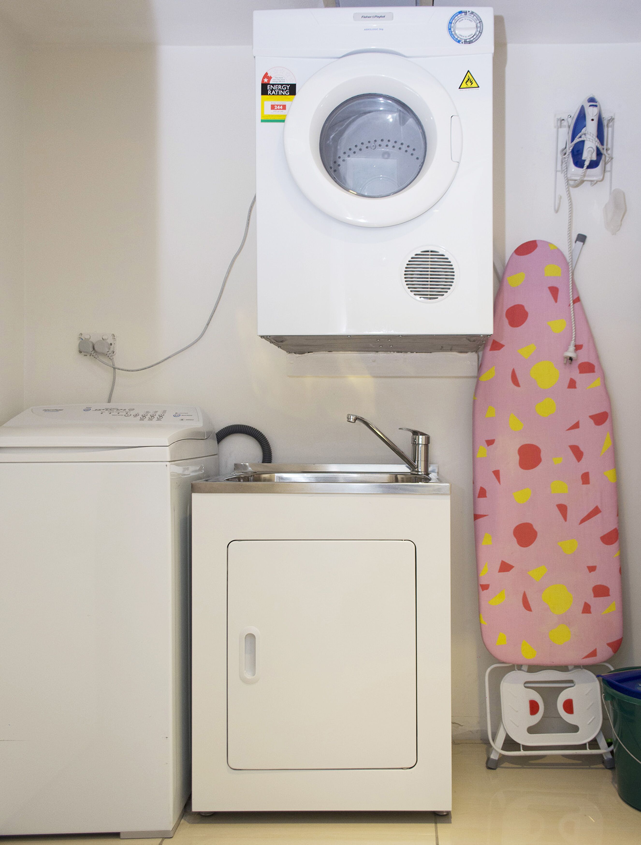 Un espacio de lavandería pequeño, con lavadora, un lavabo y una plancha.