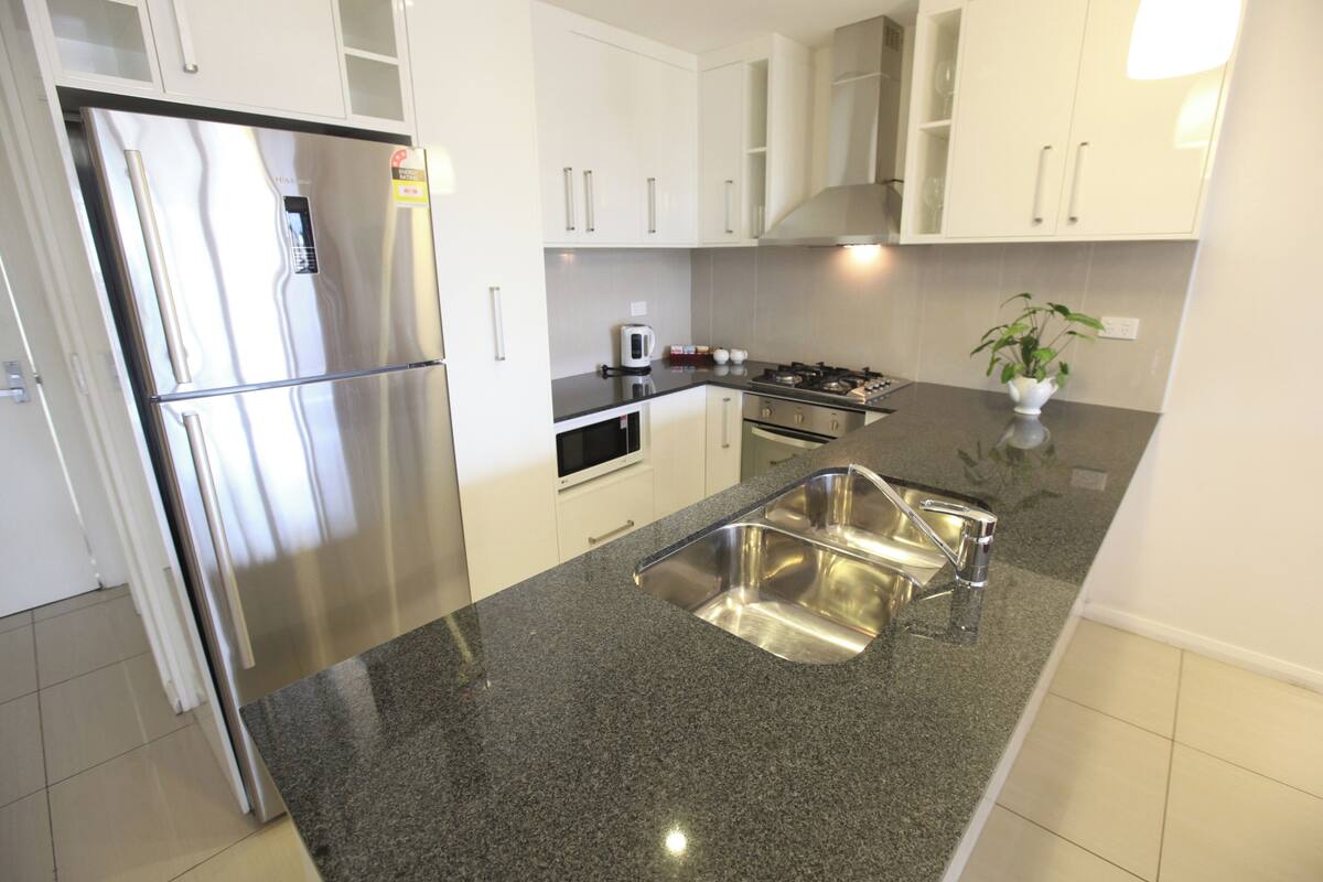 Una cocina moderna con electrodomésticos de acero inoxidable, encimera de granito y muebles de cocina blancos.