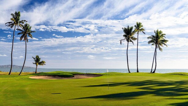 A golf course with a clear view of the ocean, palm trees, and a flagstick on the green. - Premiere Apartments (Nadi)