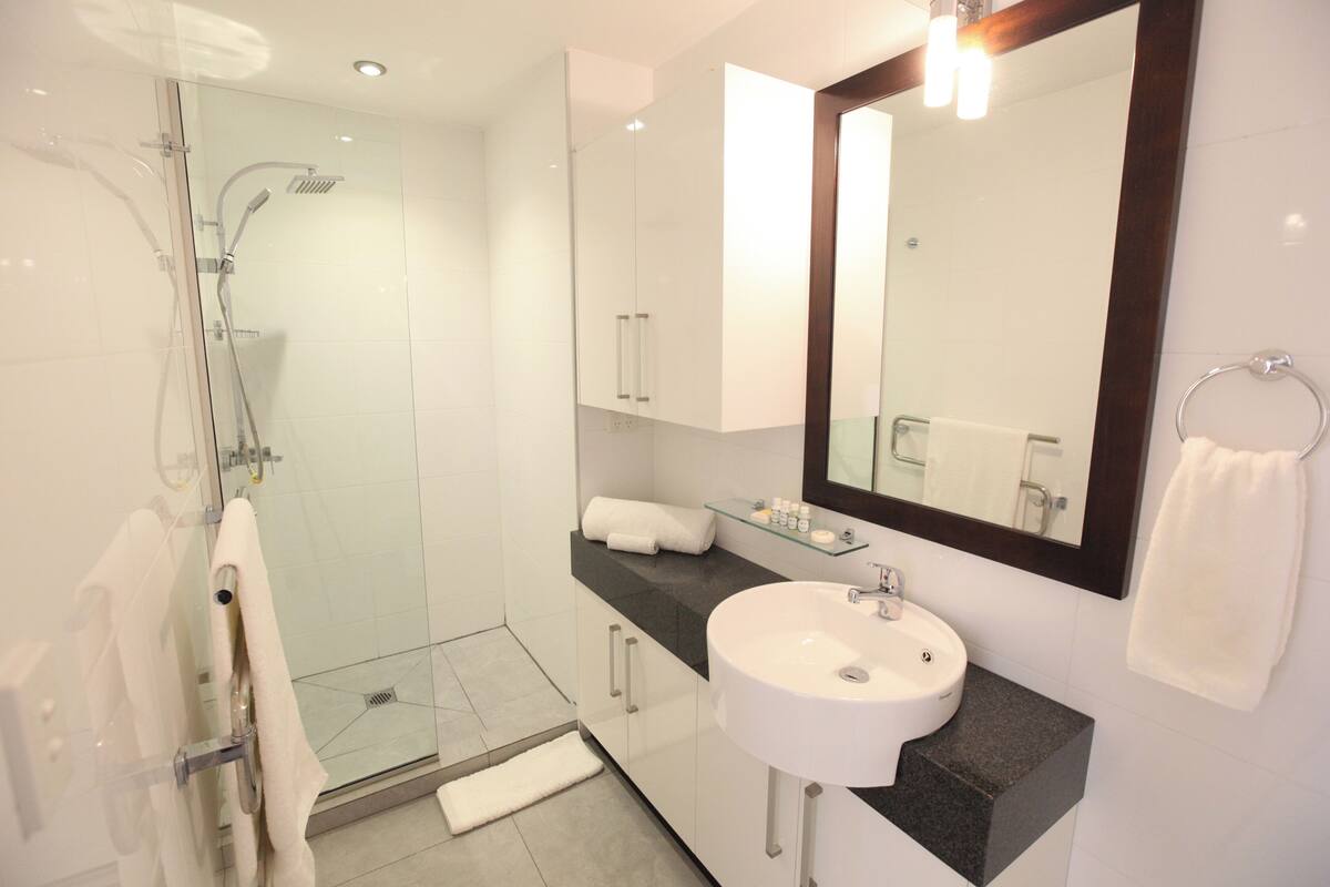 Un baño moderno con ducha envuelta en vidrio, un lavamanos blanco y un espejo grande.