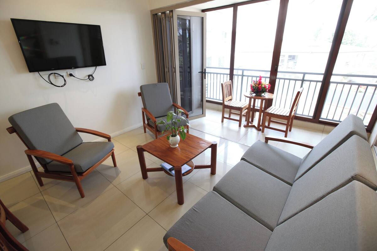 Una sala de estar con un sofá, dos sillones, una mesa de centro y un televisor montado en la pared.