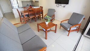 A modern living room with a sofa, two armchairs, a coffee table, and a dining area with chairs and a table. - Premiere Apartments (Nadi)