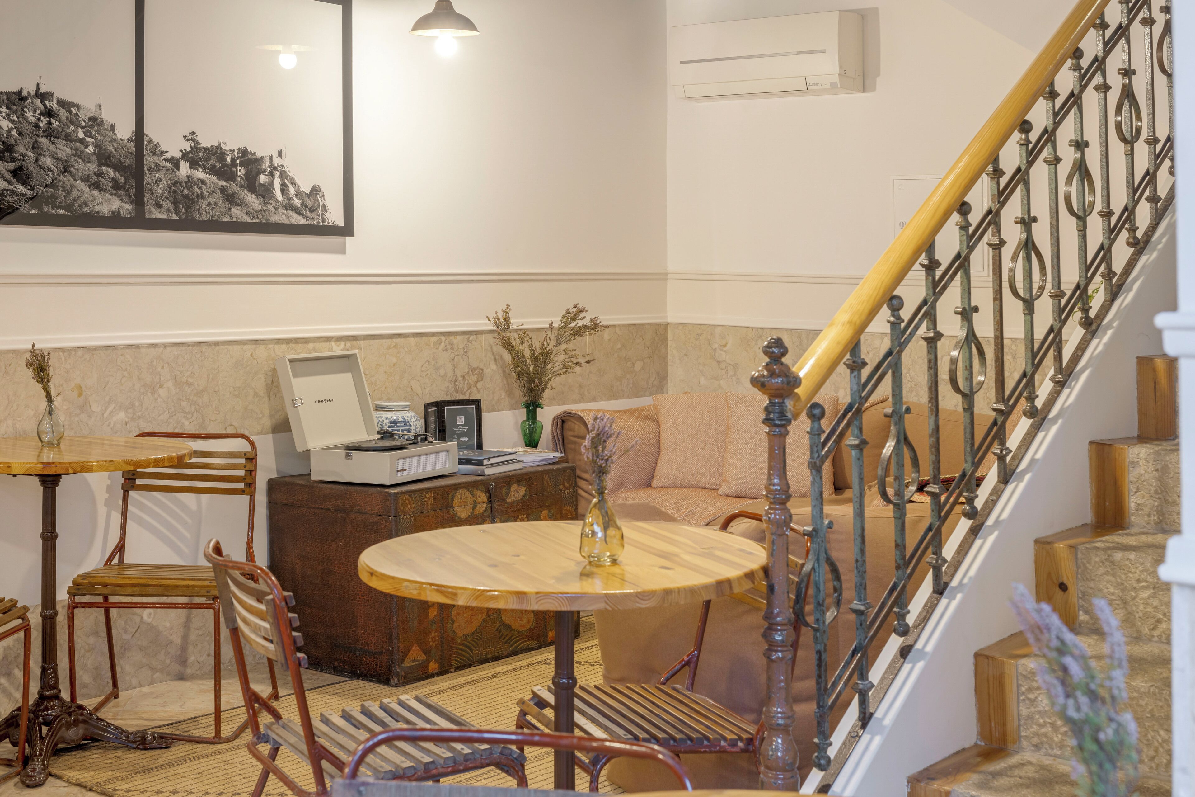 A cozy living area with a round wooden table, a sofa, and a staircase with a metal railing.