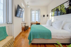 A bedroom with a bed, a TV mounted on the wall, a window, and a small table with a chair.