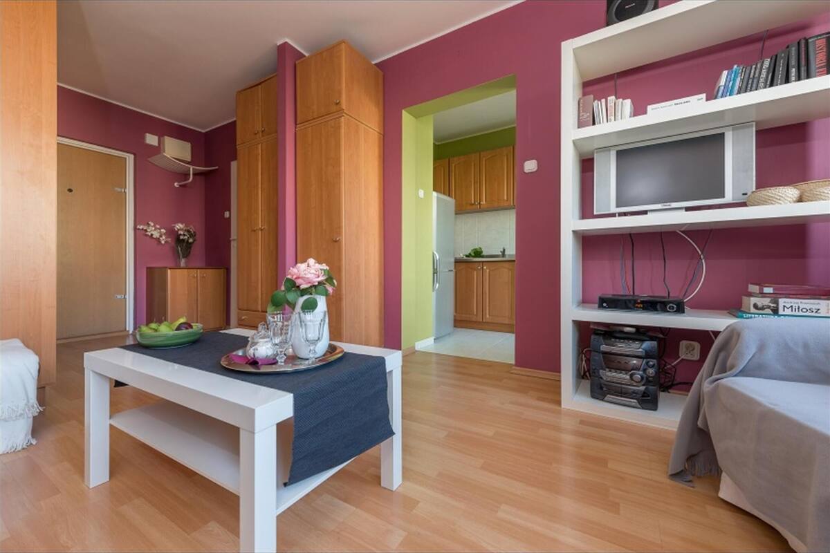 A compact living space with a dining table, a sofa, and a TV on a shelf.