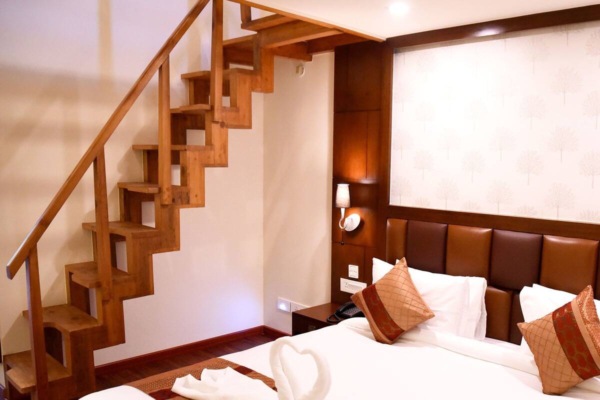 A hotel room with a wooden staircase, a large bed with white linens, and a headboard with multiple pillows.