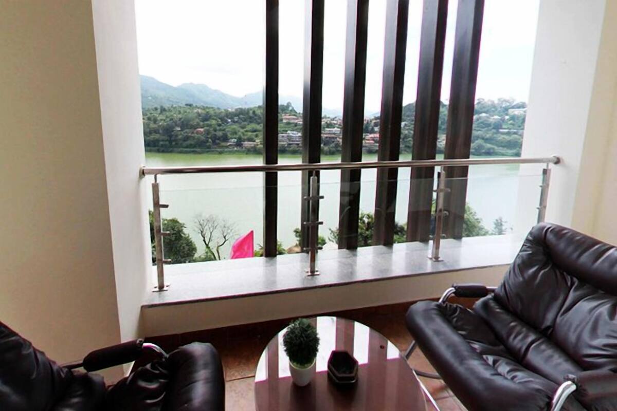A balcony with a view of a lake and mountains, furnished with leather chairs and a small table.