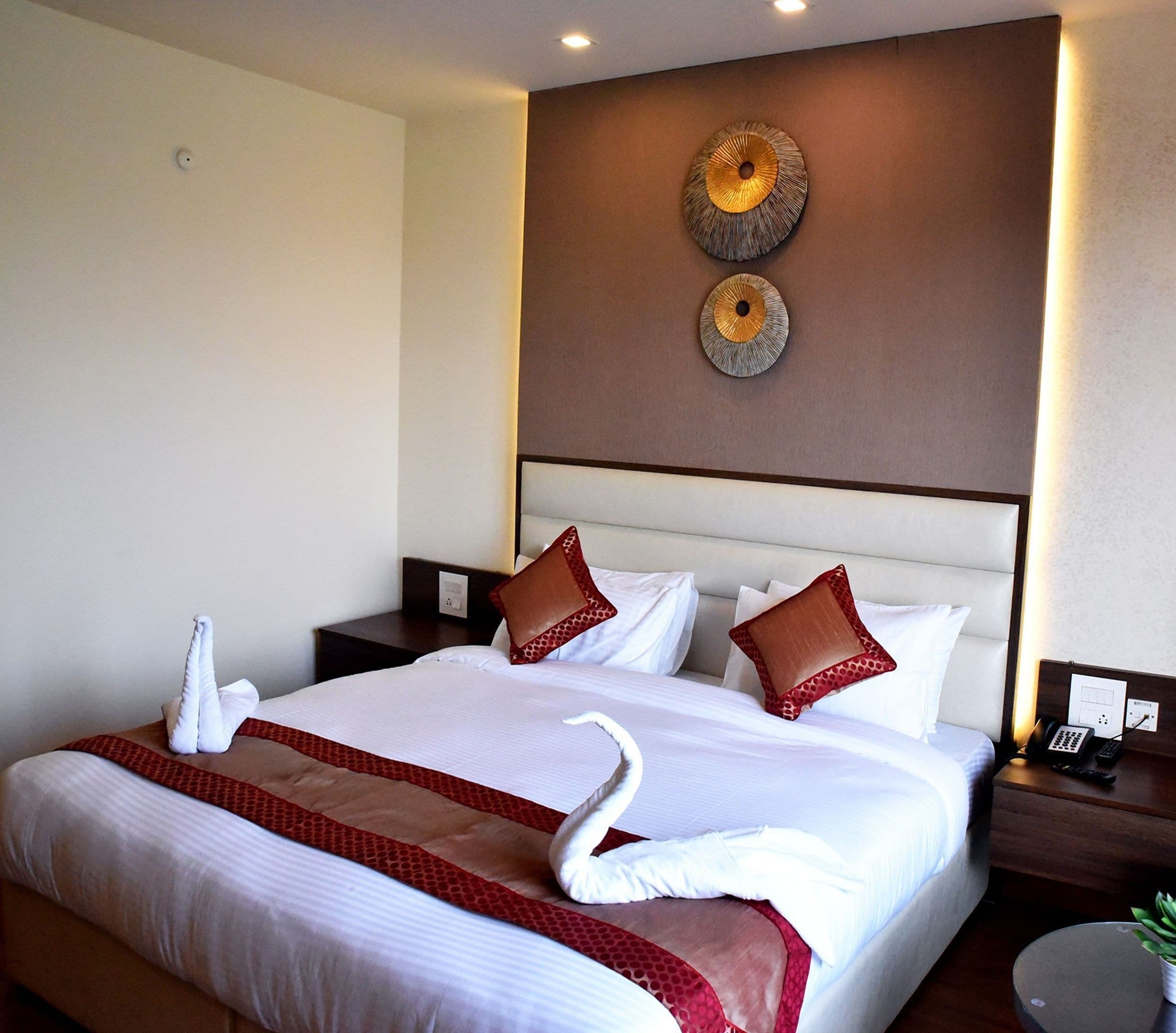 A hotel room with a large bed, two decorative wall pieces, a bedside table with a phone, and a small plant on a side table.