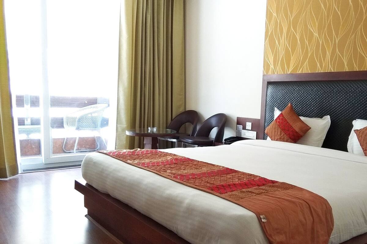 A hotel room with a large bed, a small table, two chairs, and a view of the outside through a sliding door.
