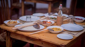 A wooden dining table set with plates, bowls, utensils, and a candle. - Apsaras Resort Sigiriya (Sigiriya)