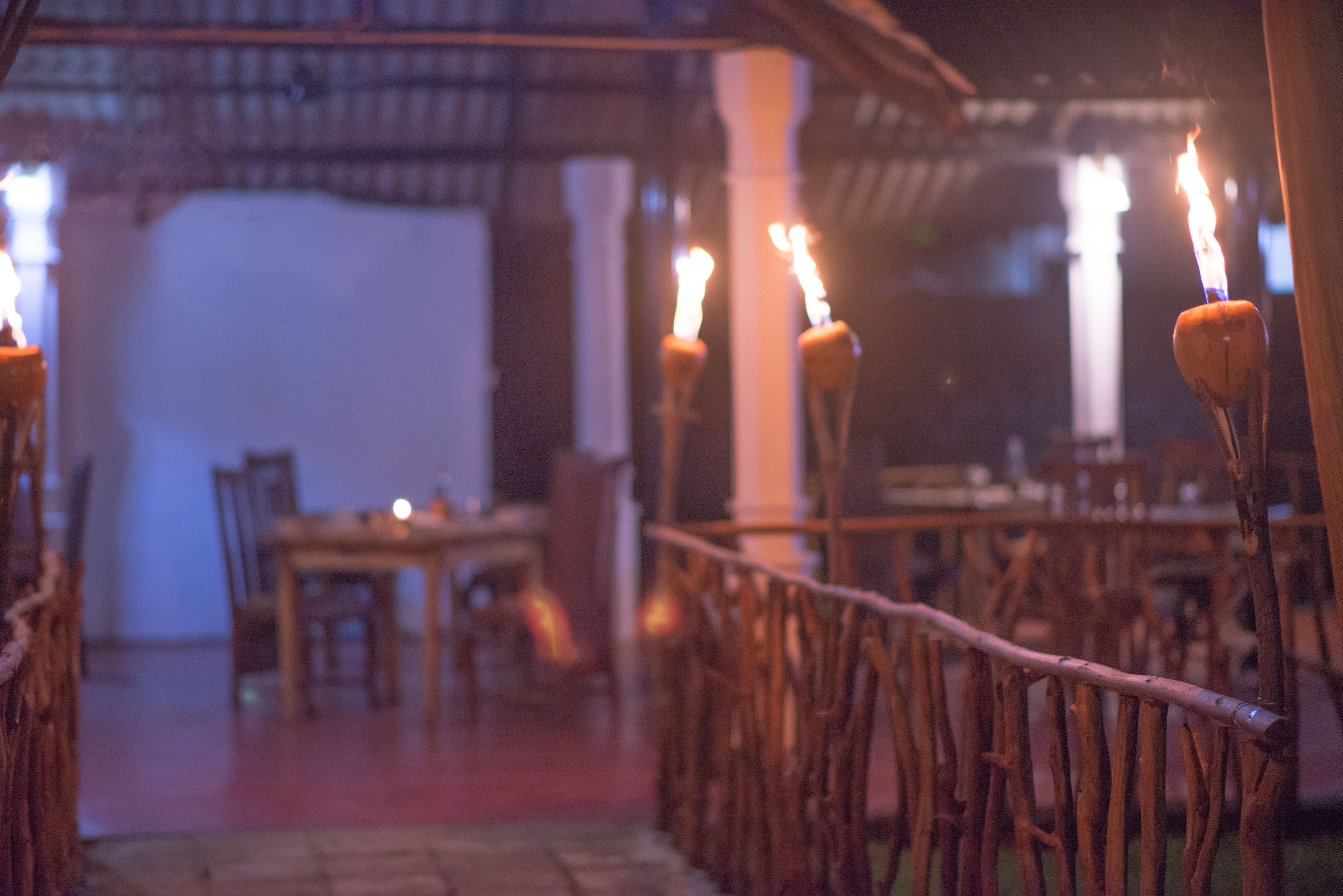 A dimly lit outdoor dining area with wooden tables and chairs, and candles on branches as a centerpiece.
