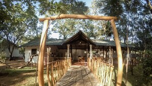 A rustic wooden walkway leading to a covered outdoor dining area with a tiled floor and a metal roof. - Apsaras Resort Sigiriya (Sigiriya)