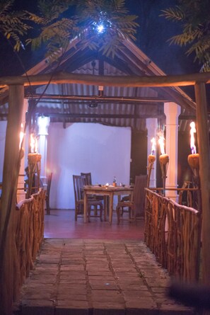 Eine hölzerne Pergola mit Tisch und Stühlen unter einem Baldachin, beleuchtet von Kerzen.